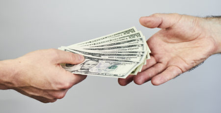 two hands exchanging dollars on grey background
